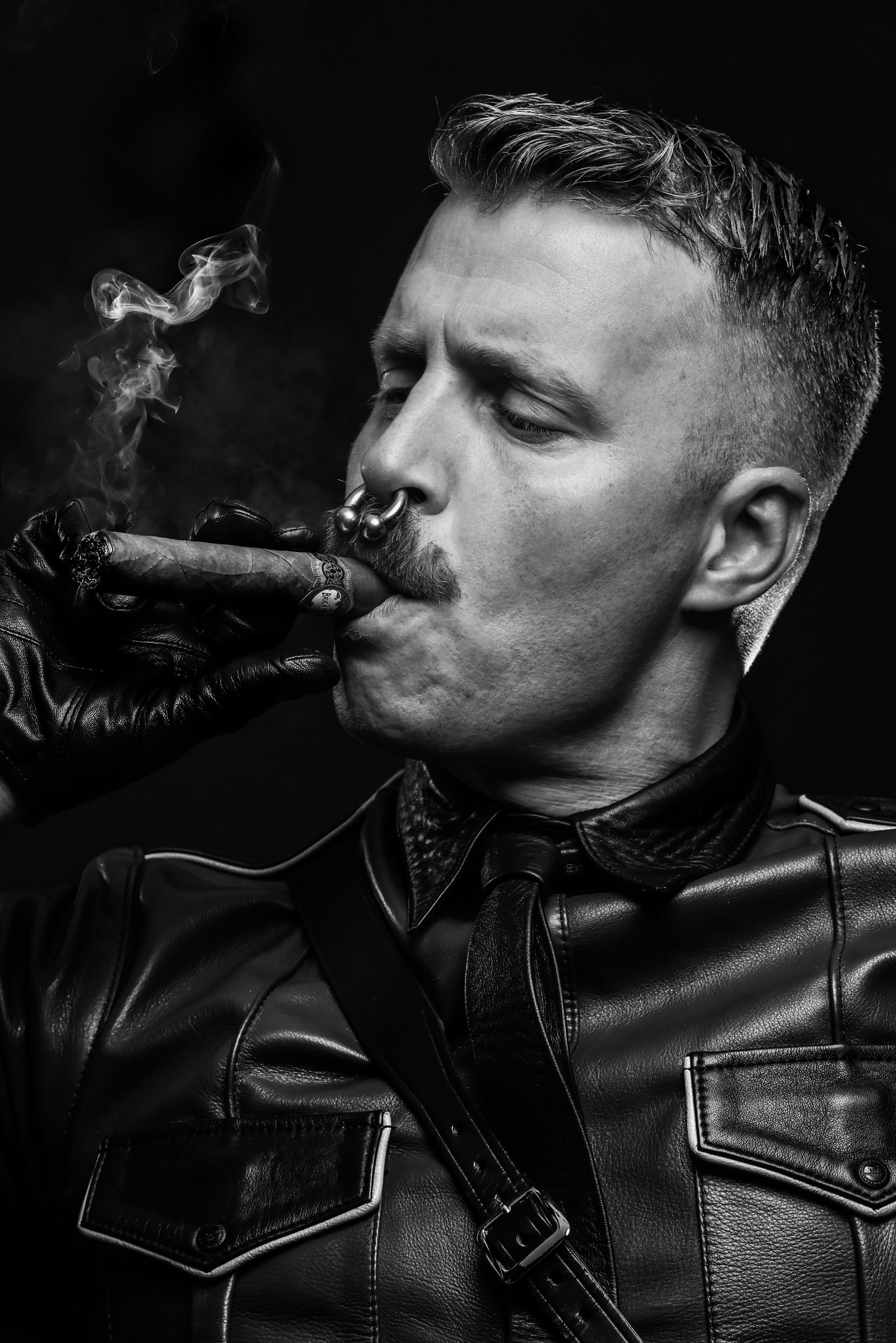 Black-and-white portrait: a broader-bodied man with a cigar lit in sculpted contrast, calm and self-assured in front of the lens.
