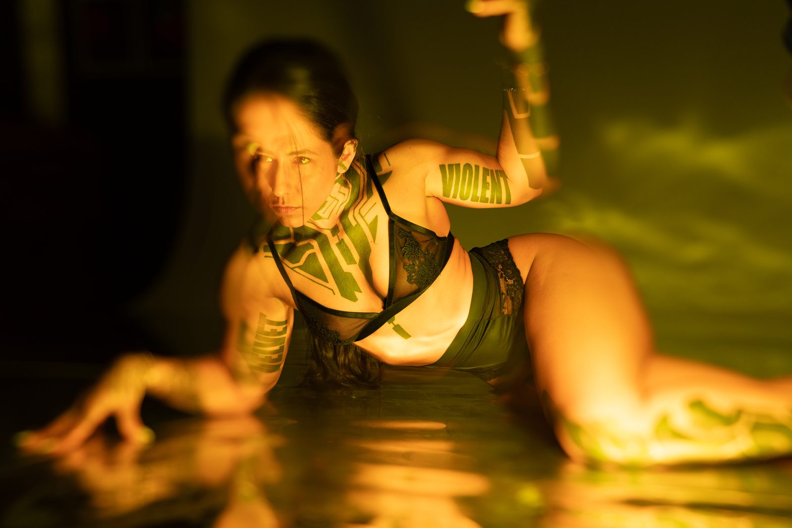 Projected amber text mapped across a reclining figure on a reflective floor, a wash of gold gel filling the frame, from the Light & Body series.