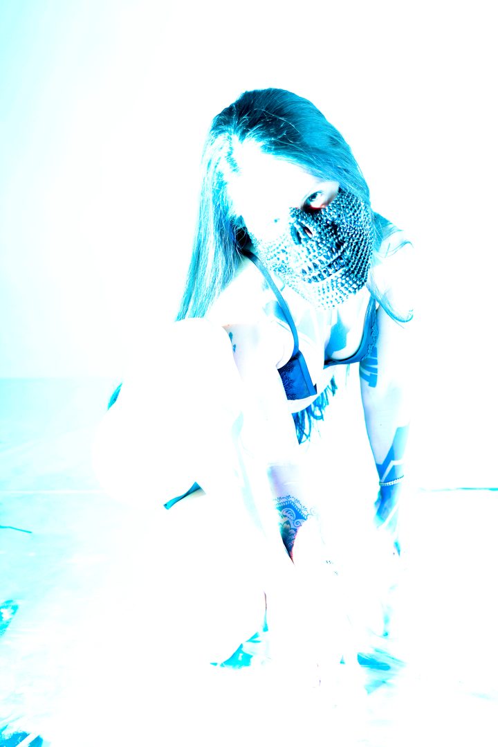 A teal-lit figure with long hair and a patterned garment, low to a reflective floor that catches the cool light.
