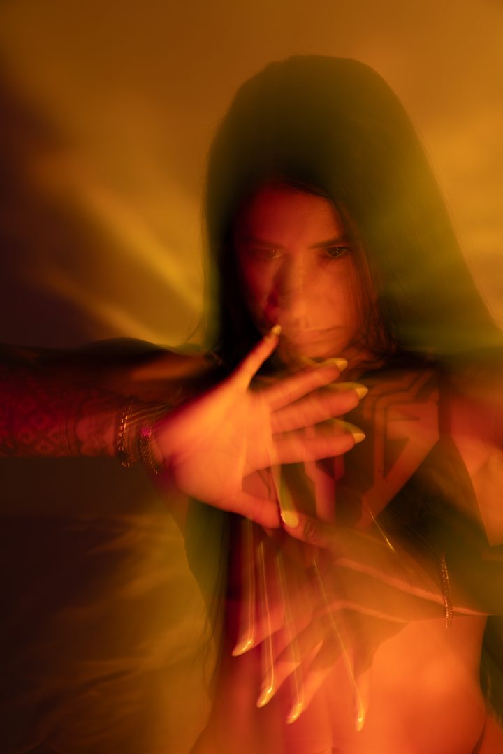 A figure in warm amber gel reaching toward the lens, the gesture trailed and softened by long-exposure motion.