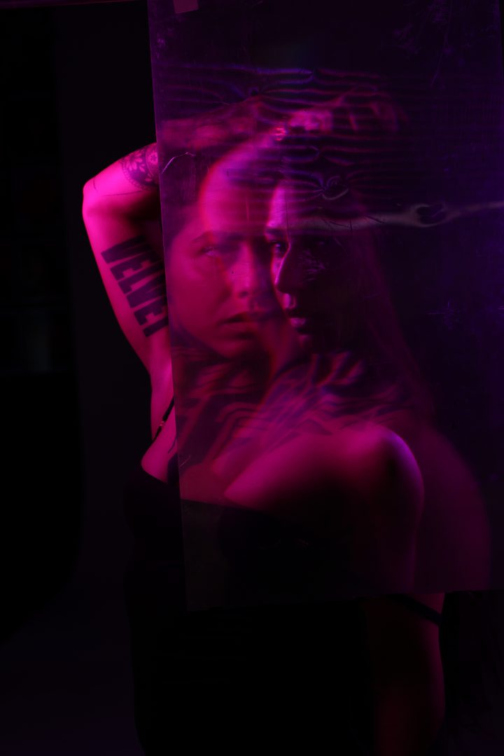A red-lit double portrait, the figure doubled and trailed by motion across a field of fine projected highlights.
