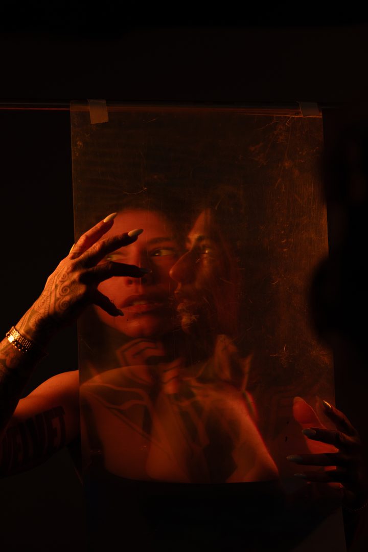 A near-abstract green frame, a figure with hands raised emerging softly from a wash of projected light and motion.