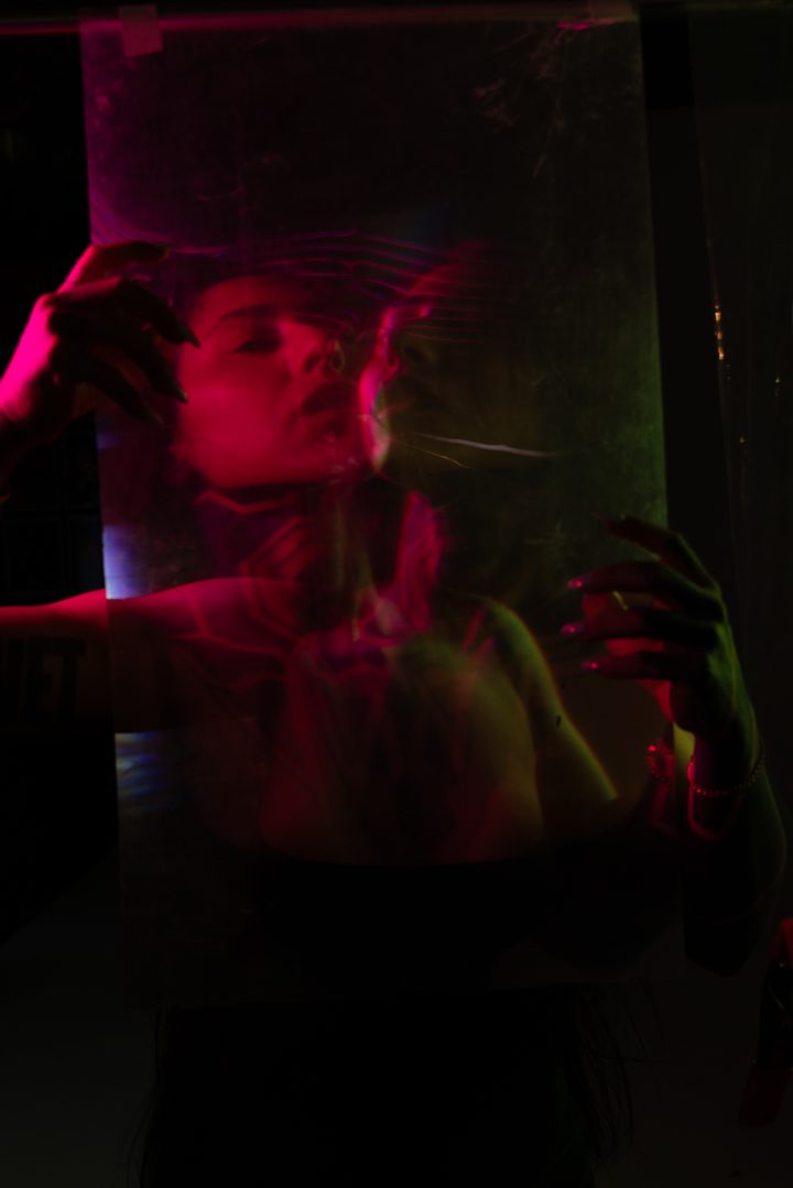 A figure pressing both hands to a sheet of acetate, the portrait doubled in red and green through the surface.